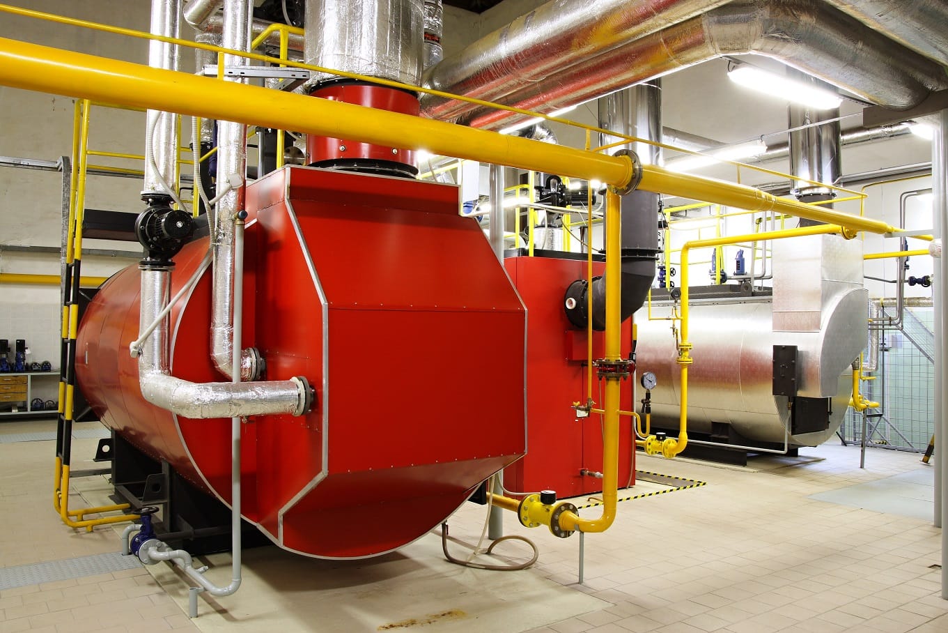 Red industrial boiler with yellow gas piping in a boiler room